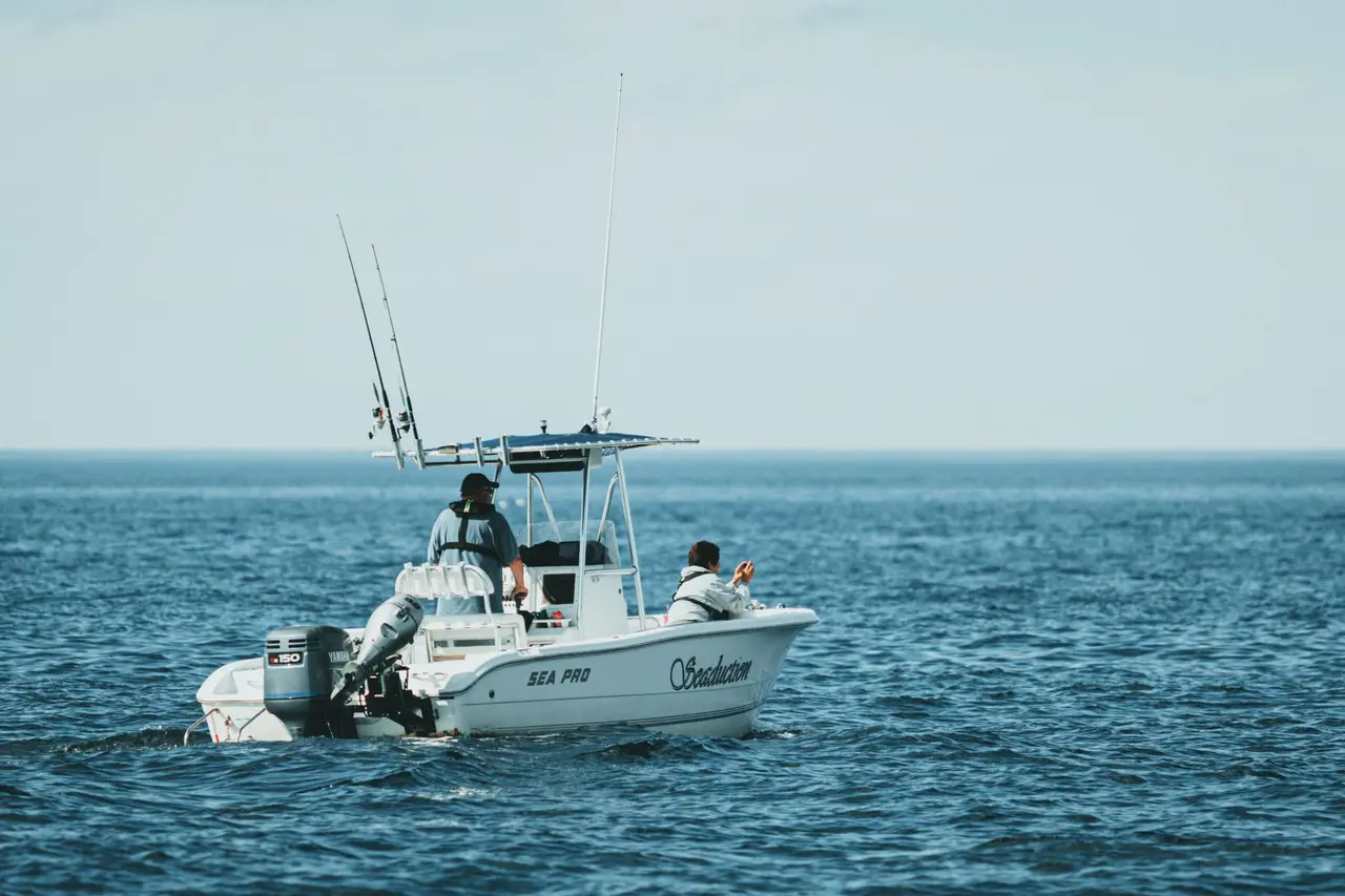 Two people on a small fishing boat with rods above blue ocean water