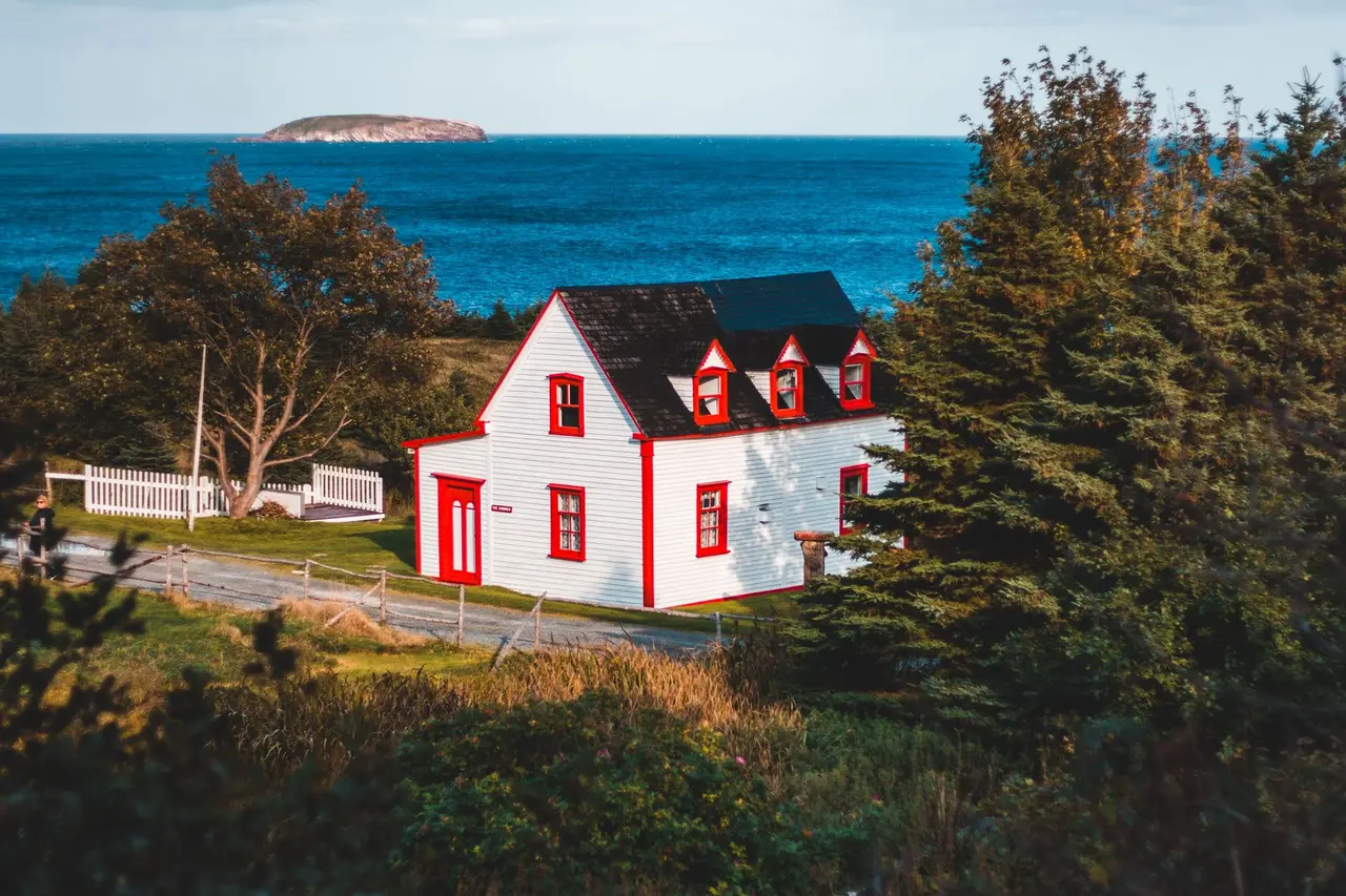 A white coastal house with a red roof and trees